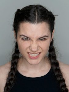 Woman with braids in her hair grimmancing facing the camera with a plain grey background