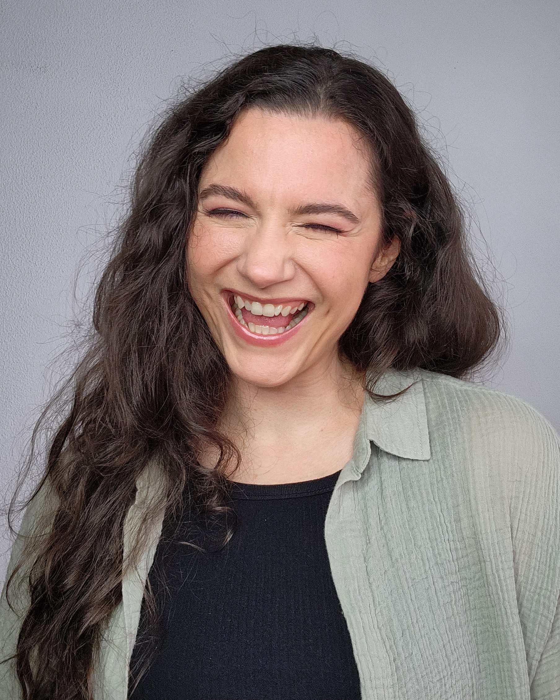 Nina Nikolic - Woman laughing with long brown hair, black top and green shirt - cartoon voice actor
