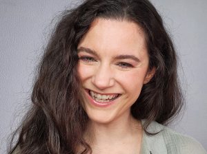 Portrait of a smiling woman with long, curly dark hair wearing a light green shirt