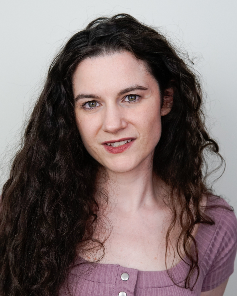 Headshot of Australian voice actor Nina Nikolic with long dark curly hair, wearing a mauve top, smiling softly against a light grey background.