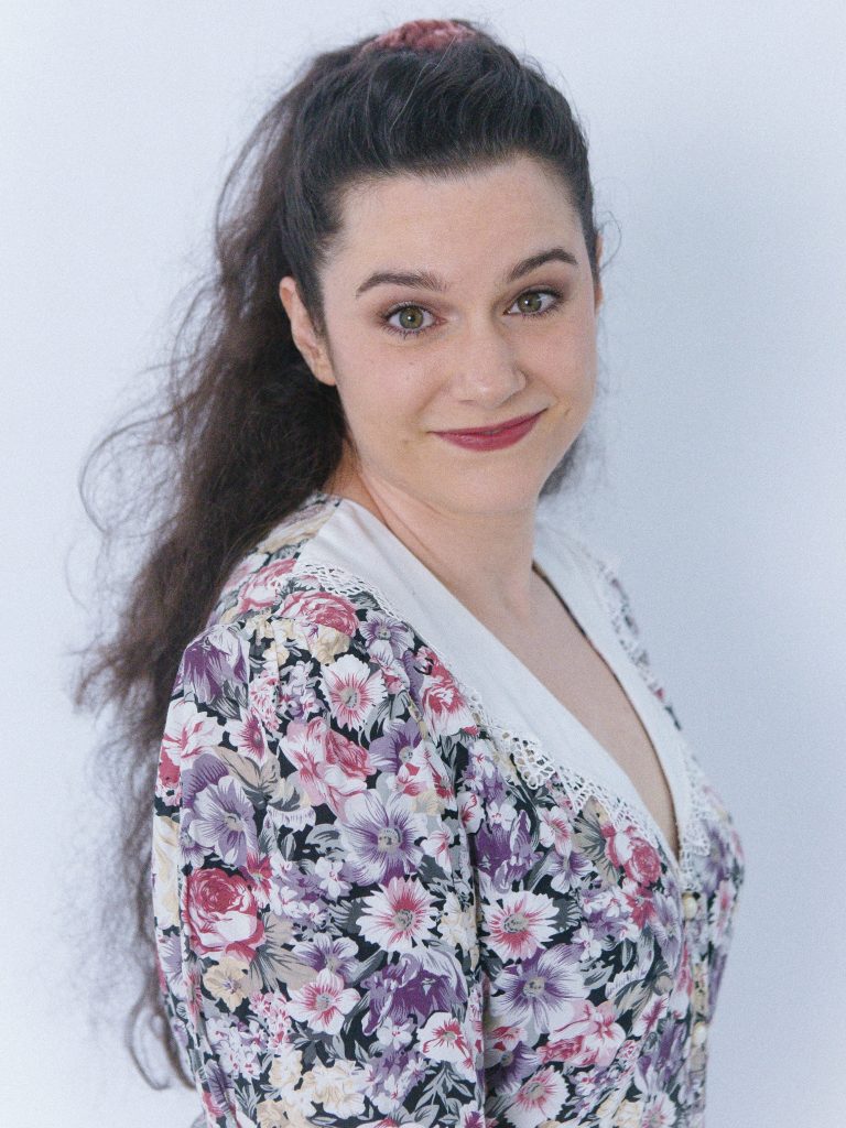 Portrait of Nina Nikolic as Dympie in After Dinner, directed by Michael Todorovic, wearing a floral blouse and looking toward the camera against a pale blue background.